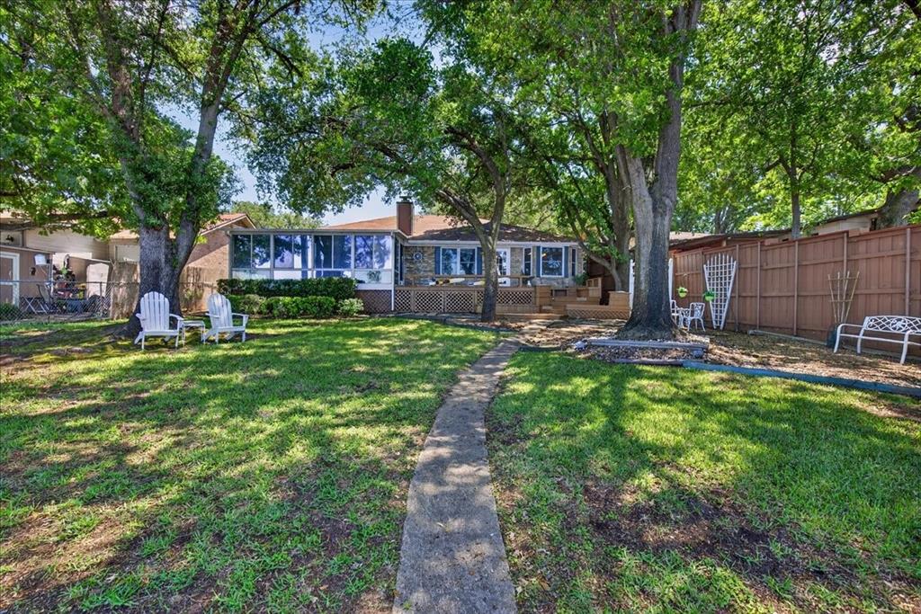 Expansive backyard featuring a stone-clad exterior, a multi-pane sunroom, mature oak trees, and a wooden privacy fence