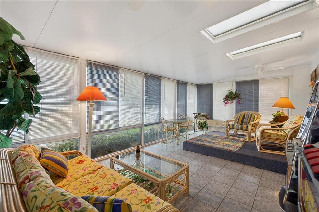 Enclosed sunroom featuring tile flooring, skylights, ceiling fans, and an extensive window wall with horizontal blinds