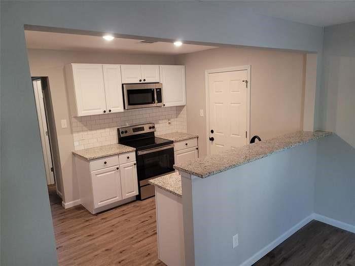 Kitchen featuring white shaker-style cabinetry, stone-finish countertops, subway tile backsplash, stainless steel appliances, and wood-finish flooring