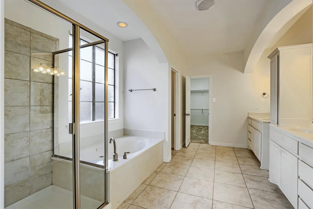 Bathroom featuring a glass-enclosed shower with tile surround, a built-in soaking tub, a dual-sink vanity with white cabinetry, and ceramic tile flooring