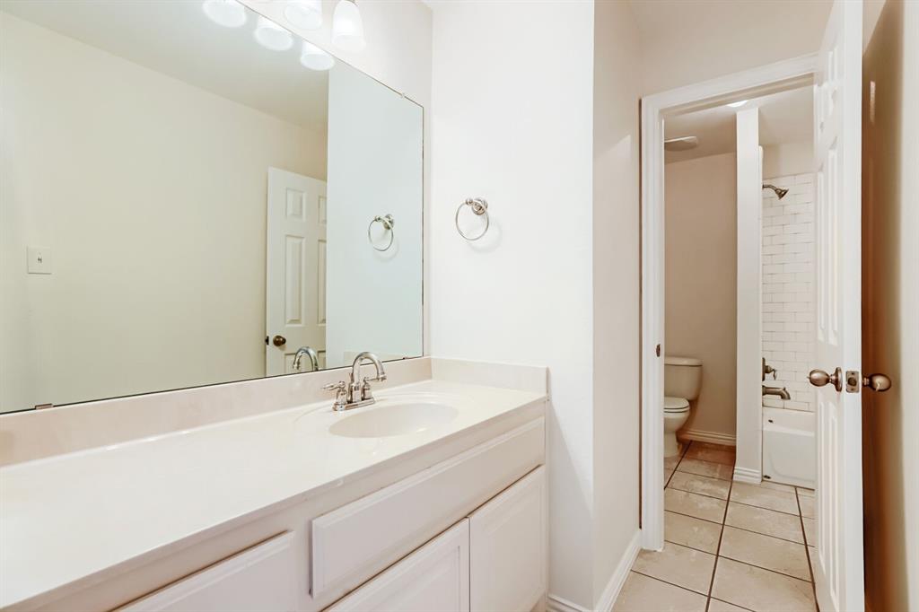 Vanity featuring a solid-surface countertop with an integrated basin, large wall-mounted mirror, polished chrome faucet, tile flooring, and a shower-tub combination with white subway-style wall tile