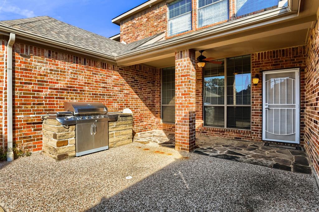 Covered brick patio featuring a built-in stainless steel grill with stone masonry surround, flagstone accents, ceiling fan, and exterior wall-mounted lighting