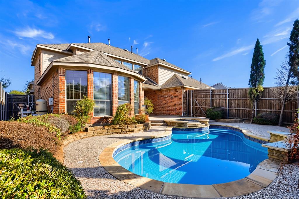 Brick exterior with a multi-gabled roofline, featuring an in-ground swimming pool with an integrated spa, stone coping, and a surrounding concrete patio