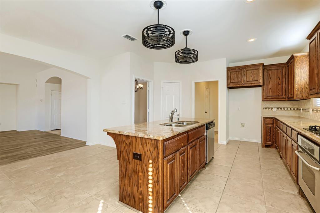 Kitchen featuring a center island, stone-finish countertops, stainless steel integrated dishwasher, custom wood-finish cabinetry, and industrial-style dual pendant light fixtures