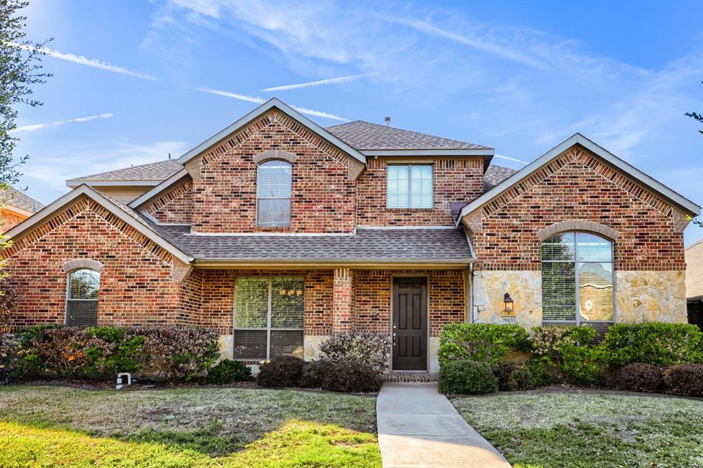 Multi-gabled brick and stone exterior featuring an arched entryway, multiple arched windows, and a concrete walkway