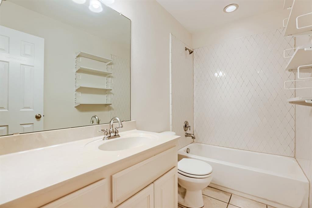 Bathroom featuring a vanity with an integrated sink, large wall-mounted mirror, white cabinetry, a tub-shower combination with diamond-patterned tile surround, and tile flooring