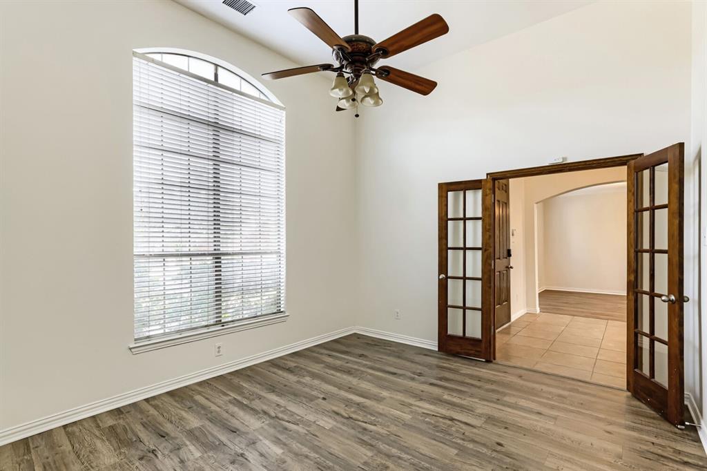 High-ceilinged room featuring wood-finish flooring, an arched window, a ceiling fan with integrated lighting, and stained wood French doors
