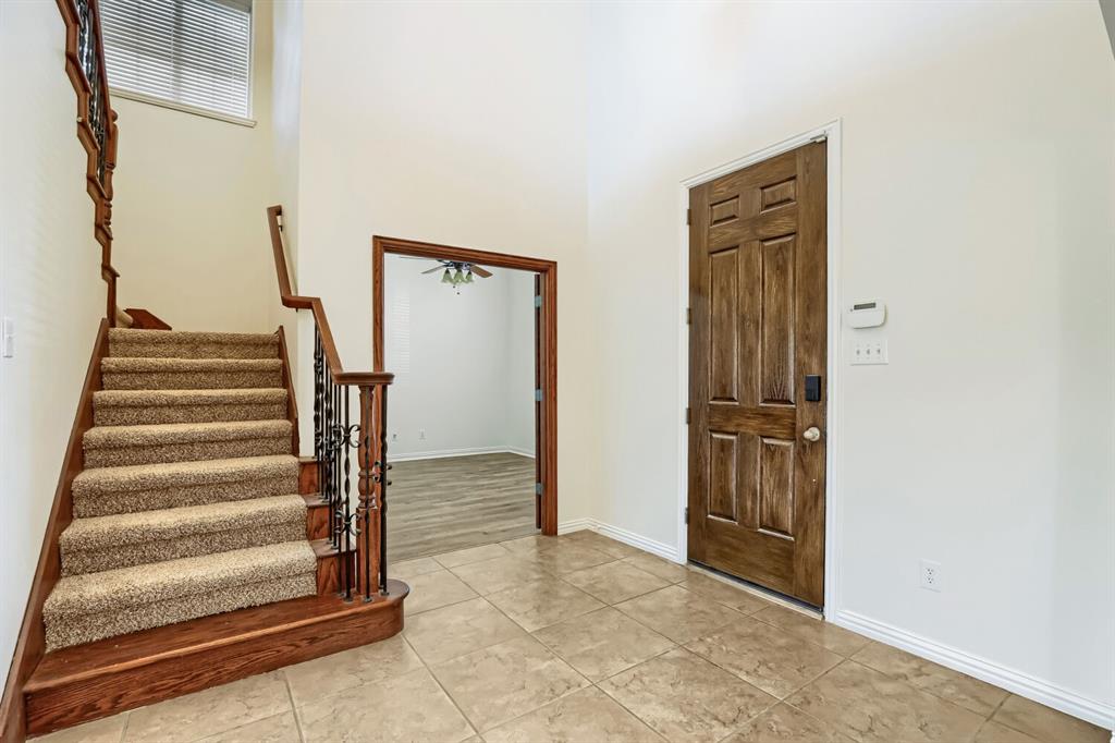 Foyer featuring high ceilings, tile flooring, a solid wood-finish entry door, and a staircase with wrought iron balusters and wood-finish railing
