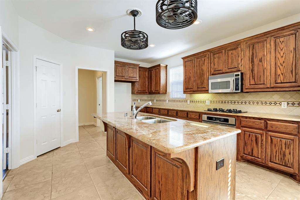 Kitchen featuring custom cabinetry, a central island with a stone countertop, built-in stainless steel appliances, decorative tiled backsplash, and dual cage-style pendant lights