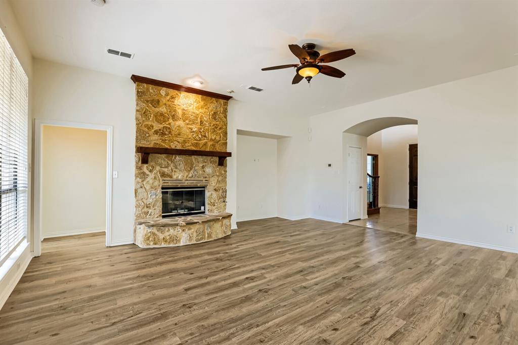 Living area featuring wood-finish flooring, vaulted ceilings, and a floor-to-ceiling stone fireplace with a wooden mantel and raised hearth, complemented by a ceiling fan with integrated lighting