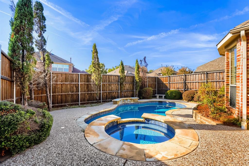 Private backyard featuring an in-ground pool with a spillover spa, natural stone coping, aggregate patio, and wood privacy fencing