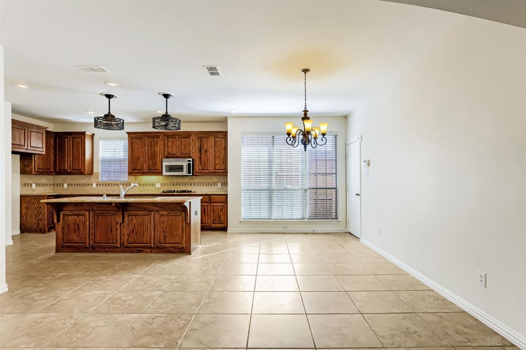 Kitchen featuring wood cabinetry, a center island with a stone-finish countertop, tile flooring, dual pendant lighting, and a multi-arm chandelier