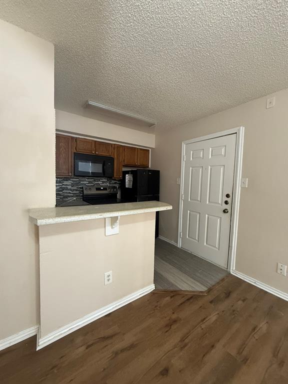 Kitchen featuring a breakfast bar with stone-finish countertop, wood-finish cabinetry, mosaic tile backsplash, and built-in microwave