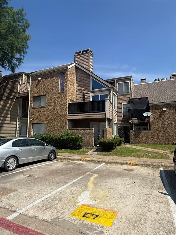 Exterior building facade featuring textured masonry siding, a gabled roofline, an elevated balcony with railing, and a chimney stack