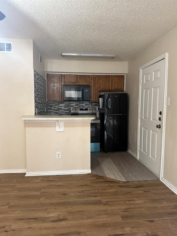 Kitchen featuring a pass-through breakfast bar, wood-finish cabinetry, a textured stone-pattern backsplash, and wood-finish flooring