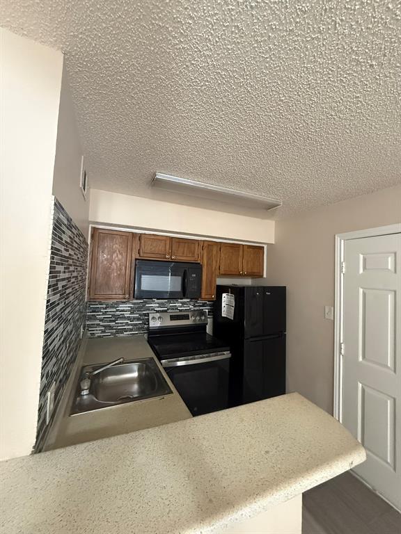 Kitchen featuring wood cabinetry, a decorative tile backsplash, stone-finish countertops, and black built-in appliances including a microwave, range, and refrigerator