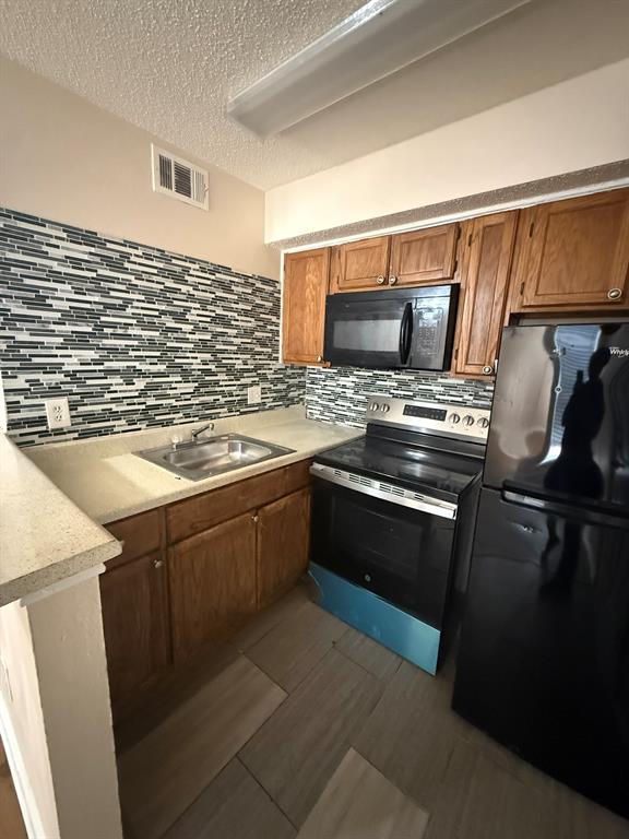 Kitchen featuring solid-wood cabinetry, stone-finish countertops, decorative multi-tonal backsplash, stainless steel sink, and black built-in appliances