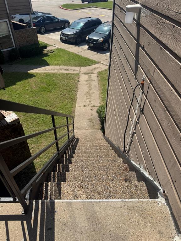 Exterior staircase with textured concrete treads, metal railing, and wall-mounted light fixture
