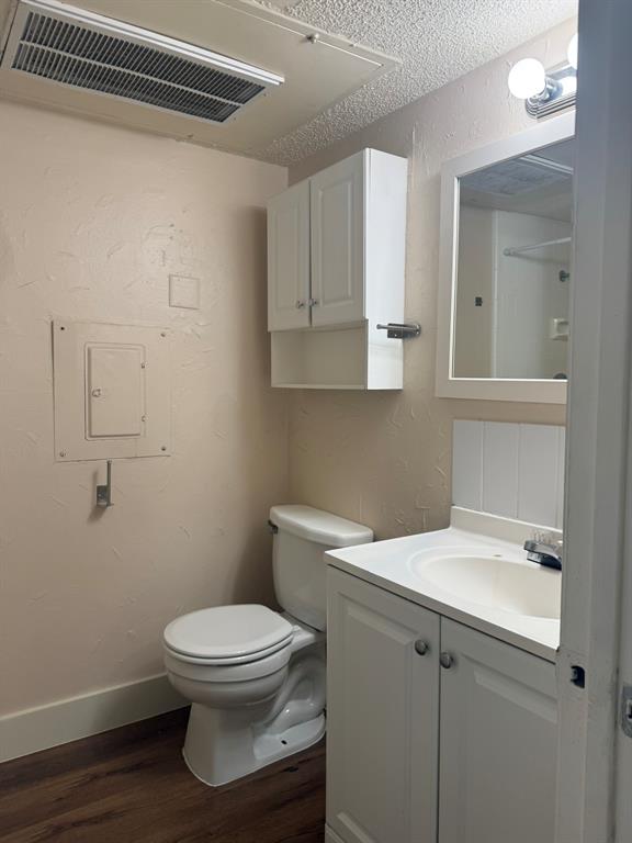 Bathroom featuring a vanity with an integrated sink, white cabinetry, wall-mounted storage cabinet, framed mirror, and wood-finish flooring