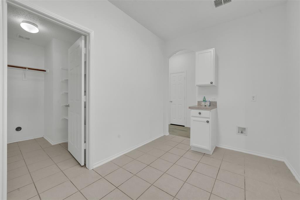 Utility space featuring tile flooring, built-in cabinetry with stone-finish countertop, and a walk-in storage area with integrated shelving