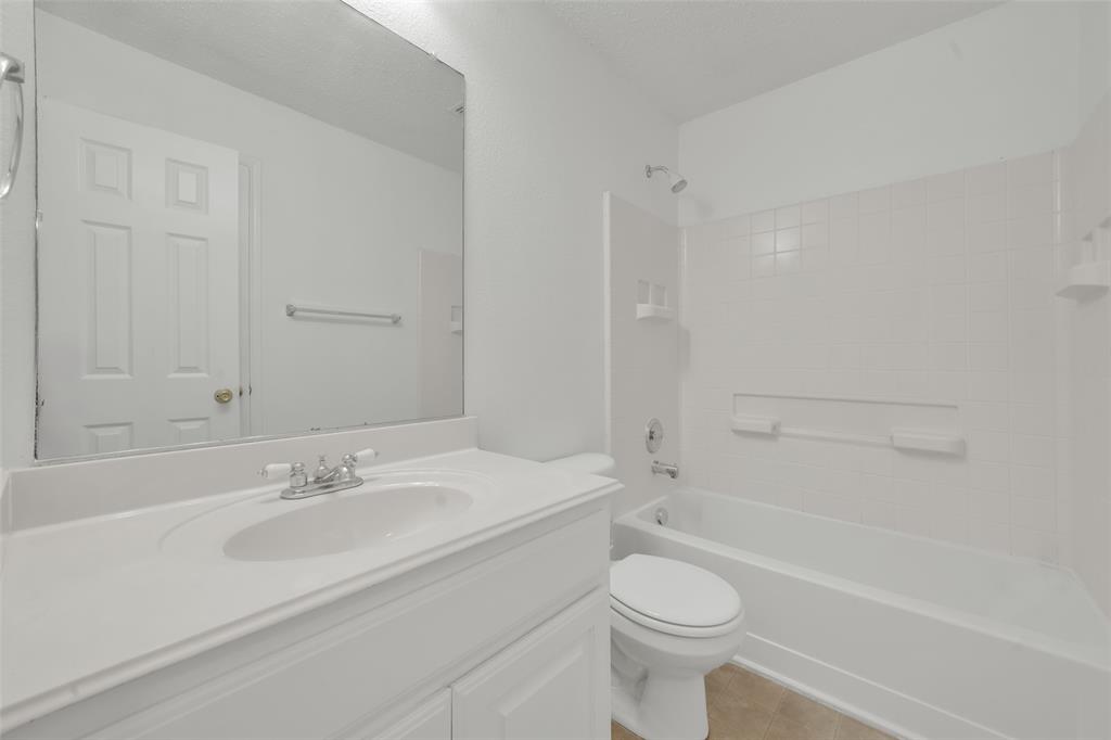 Bathroom featuring a white vanity with an integrated sink, a large wall-mounted mirror, a porcelain tub with a tiled surround, and a chrome faucet fixture
