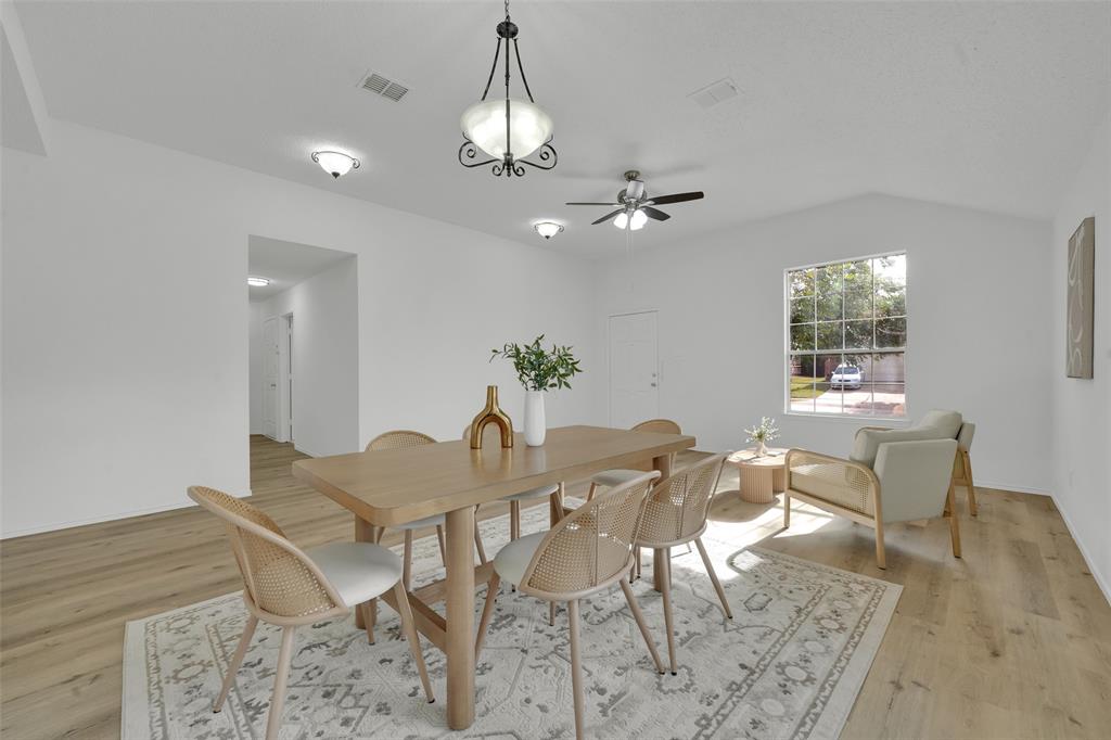 Open-concept area featuring light wood-finish flooring, vaulted ceilings, a multi-light chandelier, a ceiling fan with integrated lighting, and a multi-pane window