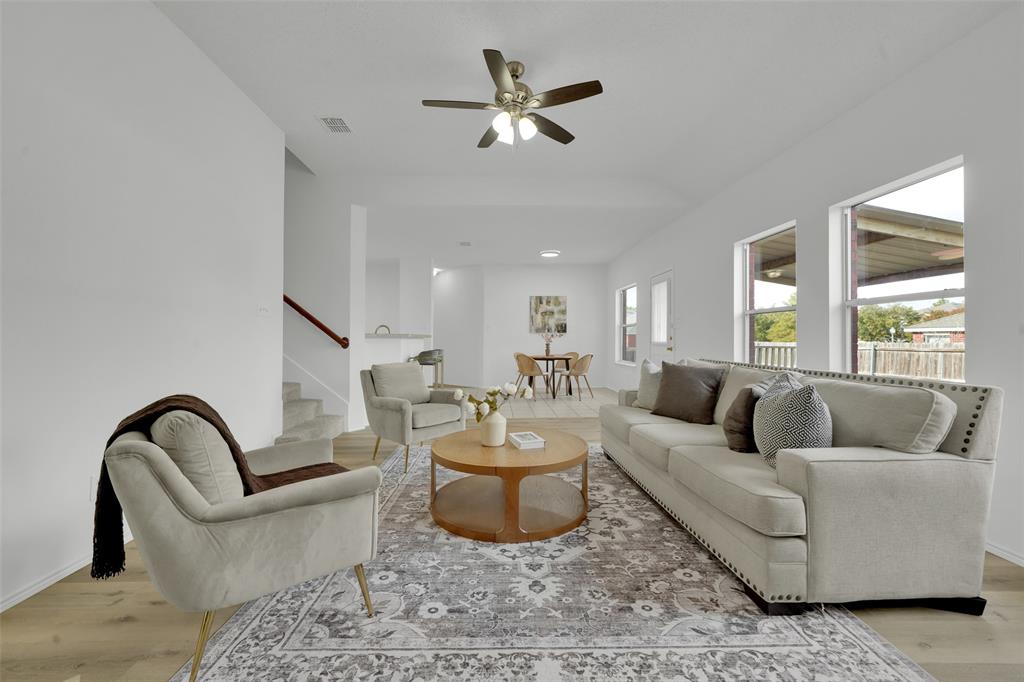 Open-concept interior featuring wood-finish flooring, neutral walls, multiple windows providing natural light, and a ceiling fan with integrated lighting