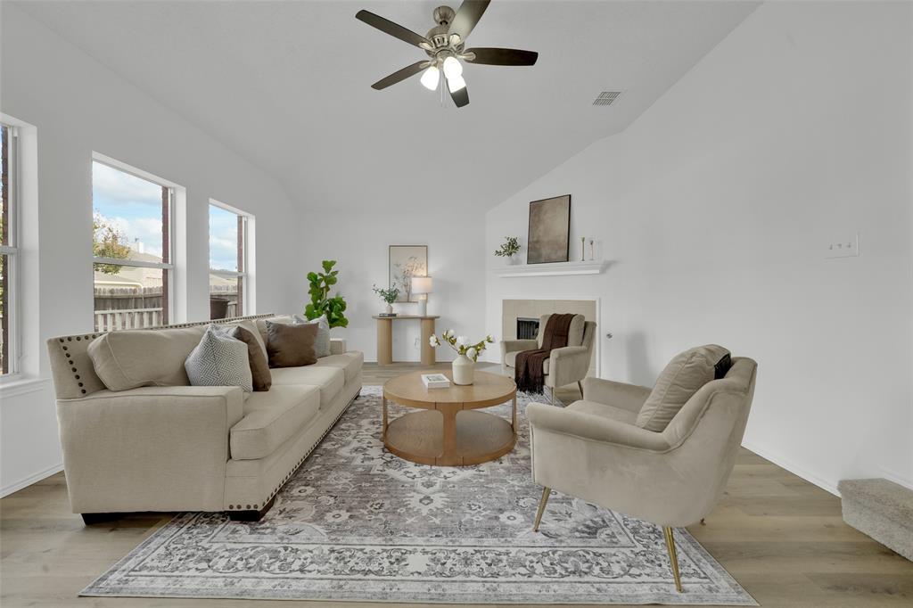 Living area featuring vaulted ceilings, wood-finish flooring, a fireplace with a mantel, and multiple tall windows