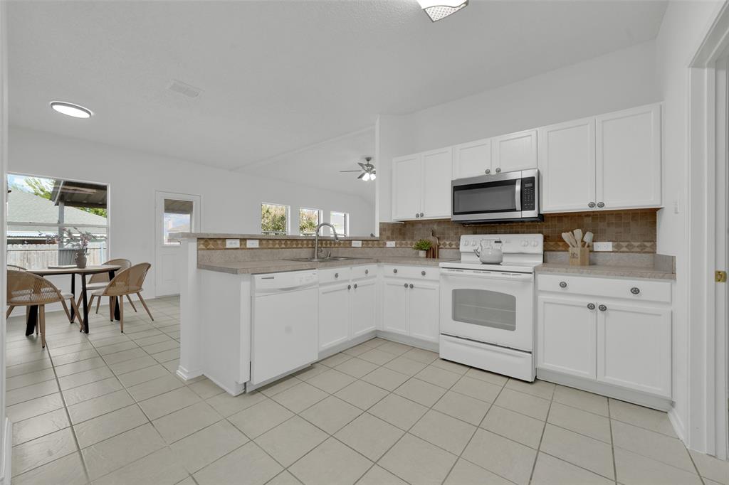 Kitchen featuring white shaker-style cabinetry, neutral-toned tiled flooring, stone-finish countertops, tile backsplash, and stainless steel microwave