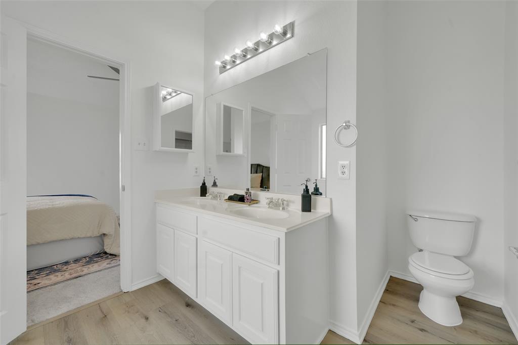 Double vanity featuring white cabinetry, integrated dual sinks, countertop with a neutral finish, expansive wall-mounted mirror, and multi-bulb light fixture