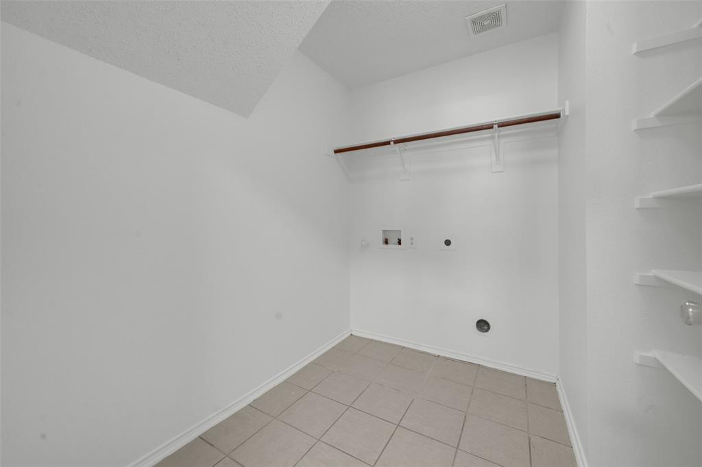 Utility area featuring ceramic tile flooring, built-in shelving, a wall-mounted hanging rod, and dedicated hookups for laundry appliances
