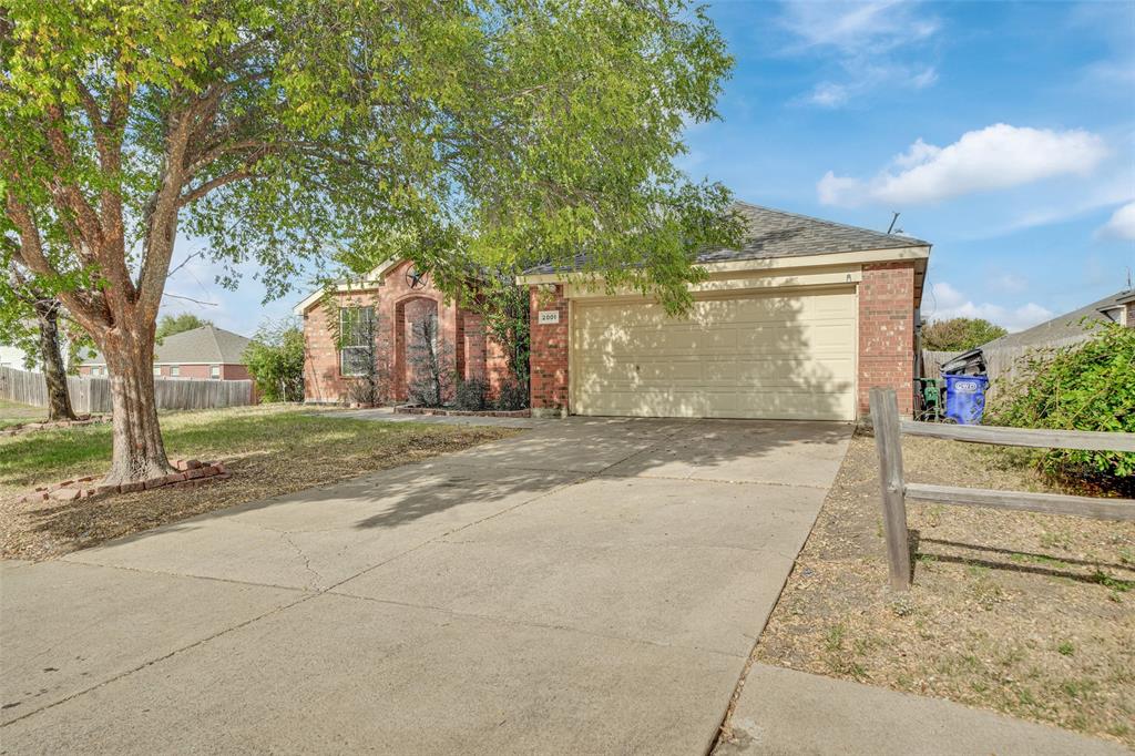 Single-story brick exterior featuring a multi-gable roofline, two-car garage, concrete driveway, and mature trees