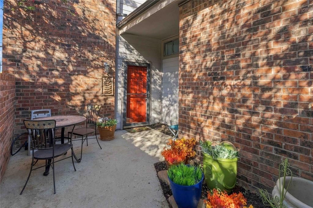 Courtyard entrance featuring a red paneled front door, brick exterior walls, and a concrete patio floor