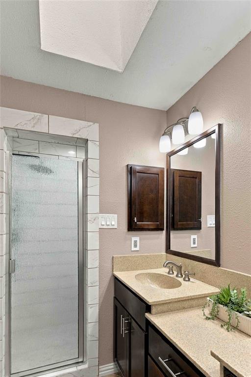 Bathroom featuring a shower stall with tile surround, skylight, built-in dark wood cabinetry, solid surface countertop with integrated basin, and a framed vanity mirror with three-light fixture