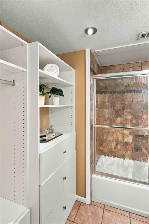 Built-in white storage cabinetry featuring open shelving and drawers, shower enclosure with tiled surround, and ceramic tile flooring