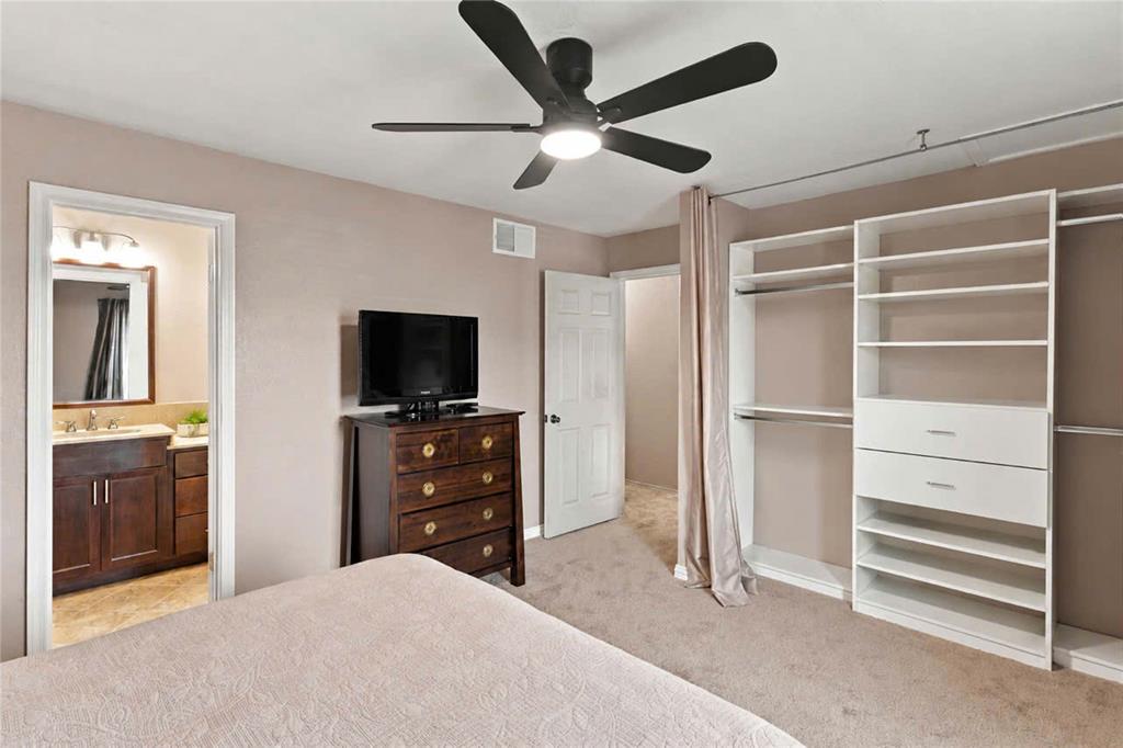 Room featuring a matte black ceiling fan with integrated lighting, wall-to-wall carpeting, and a built-in closet organization system with shelving and drawers