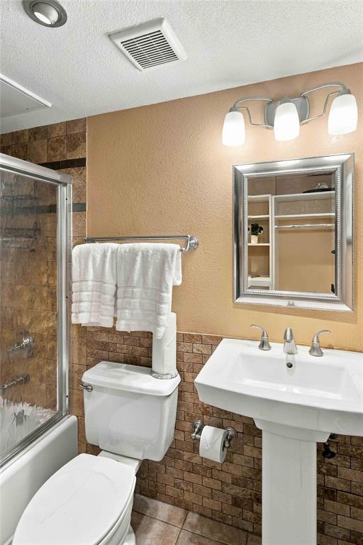Pedestal sink with polished metal faucet, glass-enclosed shower with tiled surround, and three-light wall-mounted fixture