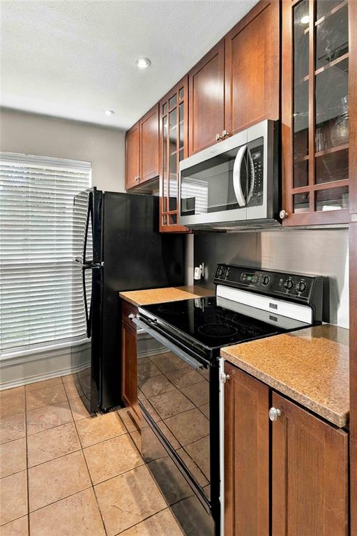 Kitchen featuring wood cabinetry with glass-paneled uppers, stone-finish countertops, tile flooring, and stainless steel microwave