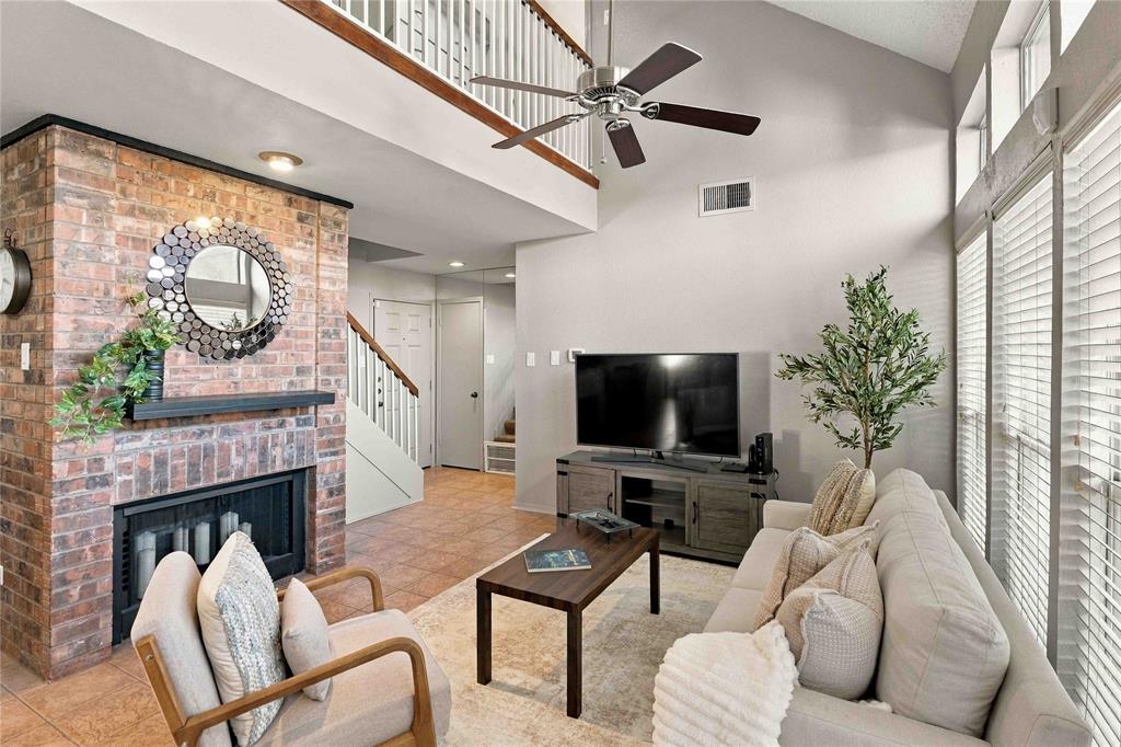 Vaulted ceiling, brick fireplace with a mantel, ceiling fan, and large windows with horizontal blinds