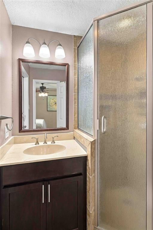 Bathroom featuring a dark wood-finish vanity, light-toned countertop with integrated oval basin, three-light wall fixture, framed mirror, and walk-in shower with textured glass enclosure