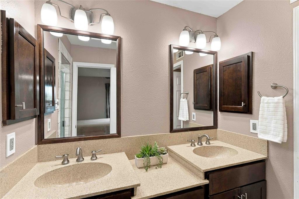 Dual-sink vanity featuring stone-composite countertops, dark wood-finish cabinetry, matching framed mirrors, and wall-mounted tri-light fixtures