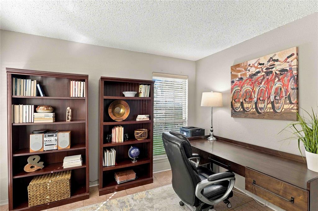 Built-in wall-to-wall wood-finish desk featuring a drawer with dark hardware, paired with two matching tall wood-finish shelving units and horizontal window blinds