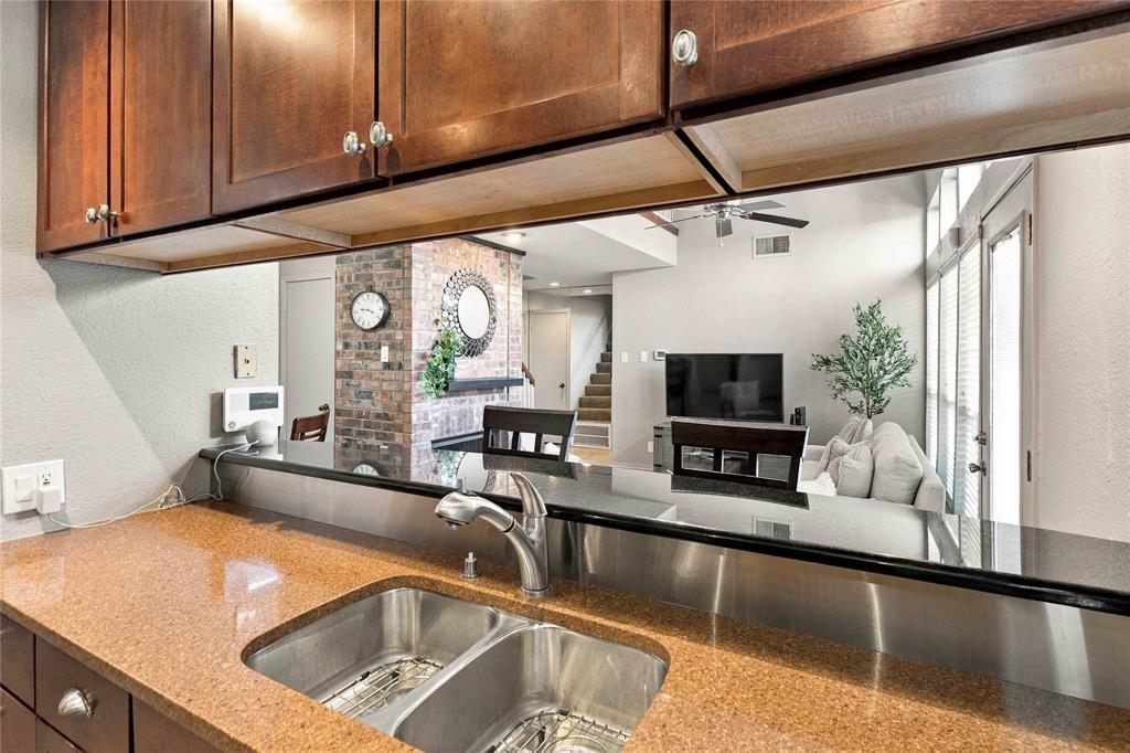 Kitchen featuring dark wood-finish cabinetry, stone countertop, dual-basin stainless steel sink with pull-down faucet, and stainless steel backsplash