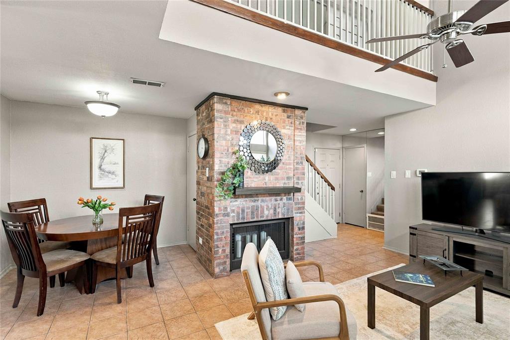 Double-height ceiling, brick-surround fireplace, tile flooring, and metal railing mezzanine