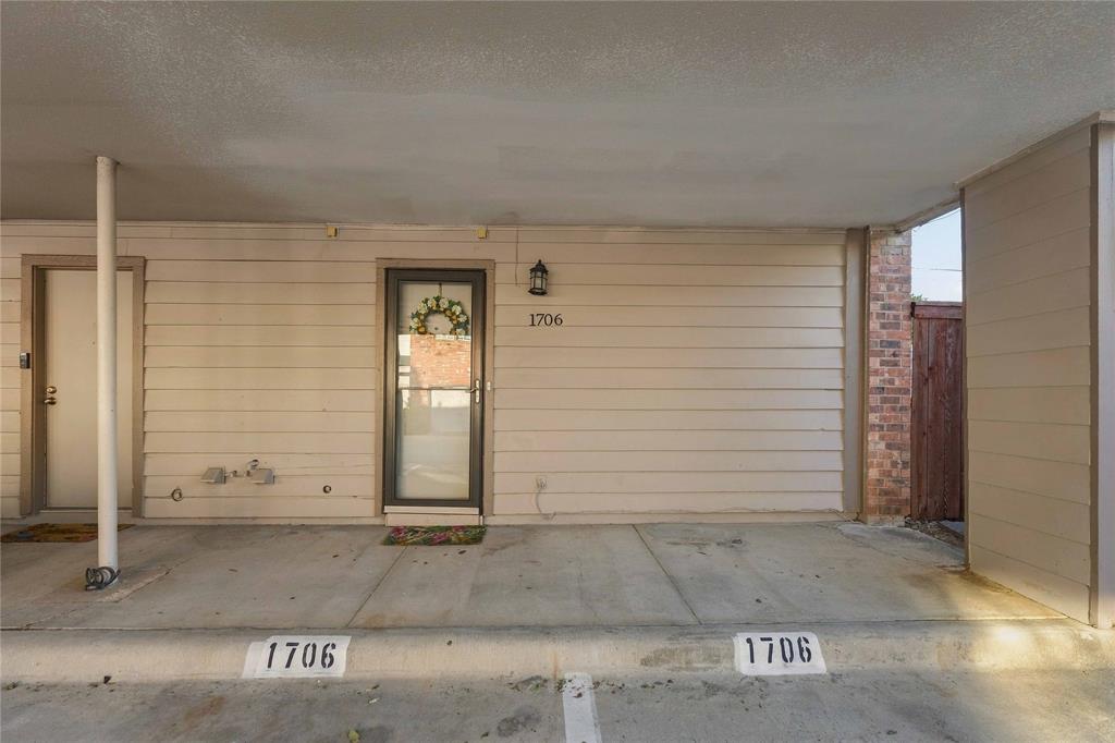 Covered carport entrance featuring horizontal siding, concrete flooring, exterior wall-mounted lighting, and a glass-paneled entry door