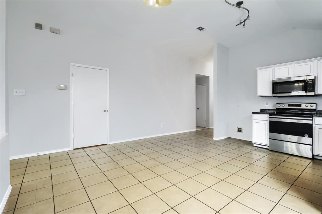 Kitchen featuring white cabinetry, stainless steel appliances, tile flooring, vaulted ceilings, and multi-light fixtures