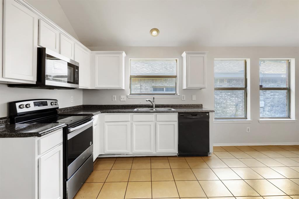 Kitchen featuring white shaker-style cabinetry, stone-finish countertops, stainless steel appliances, ceramic tile flooring, and a vaulted ceiling