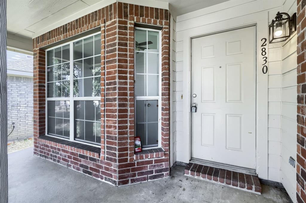 Covered entry featuring a brick-accented exterior, multi-pane windows, a paneled door, and an exterior wall-mounted light fixture