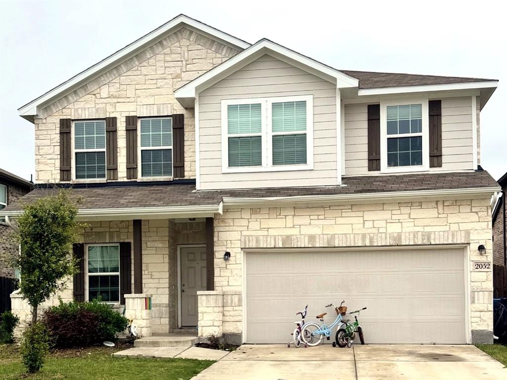 Two-story exterior featuring a mix of light-toned stone masonry and horizontal siding, decorative shutters, a multi-gabled roofline, and an attached two-car garage
