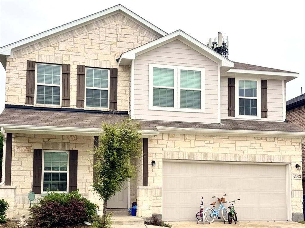 Two-story exterior featuring light-toned stone masonry, horizontal siding, decorative shutters, and an attached two-car garage